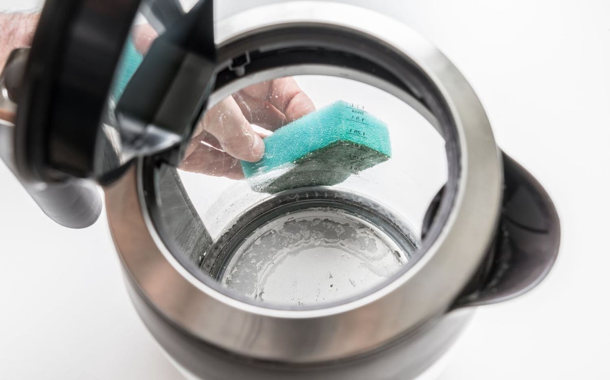 Person cleaning limescale build up from a kettle due to hard water
