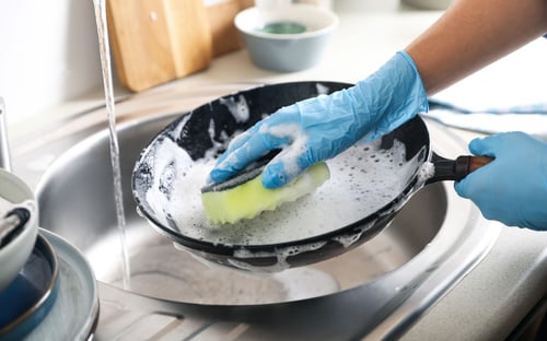 Person cleaning a pan with soapy water over a sink